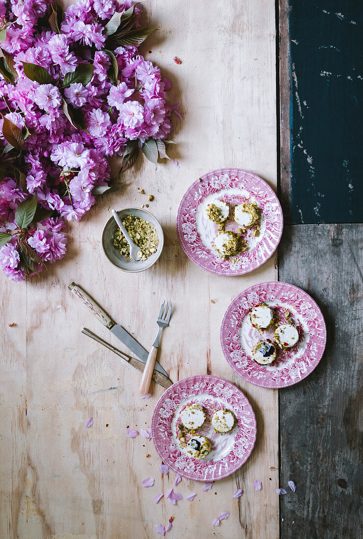 Pistachio goatcheese with rose petals on French plates with pink blossom on a wooden background