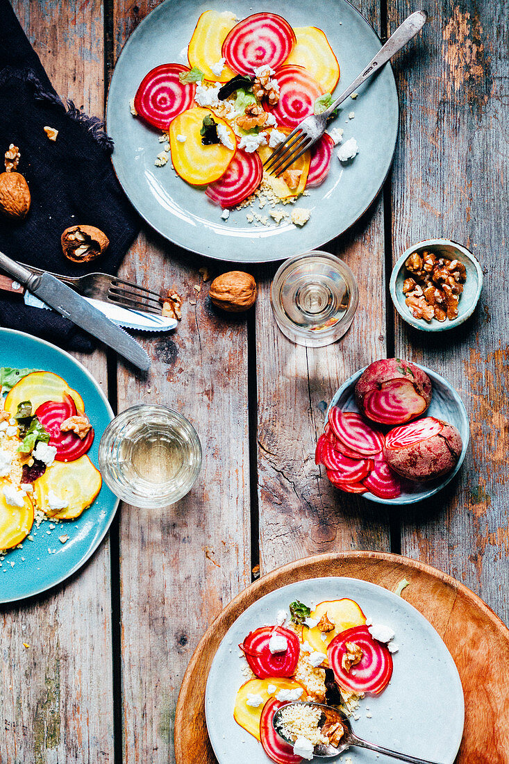 A wooden table with 3 plates with couscous, feta, lettuce, walnuts and beetroot