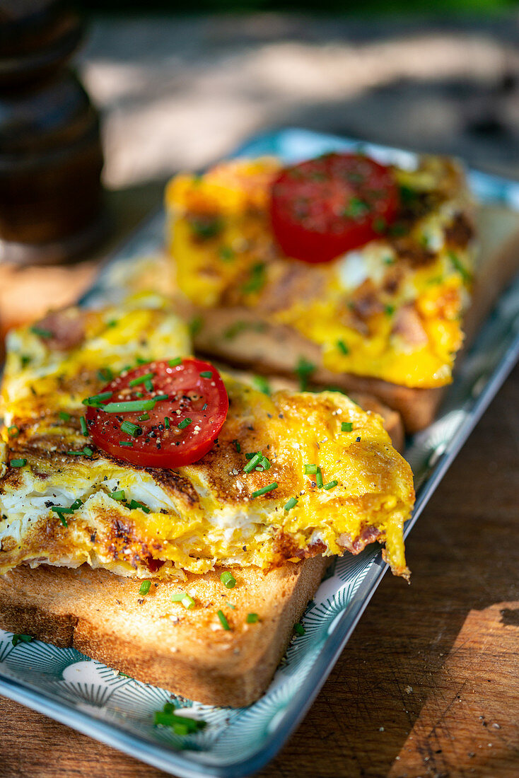 Toast with scrambled eggs, tomatoes and chives on a garden table