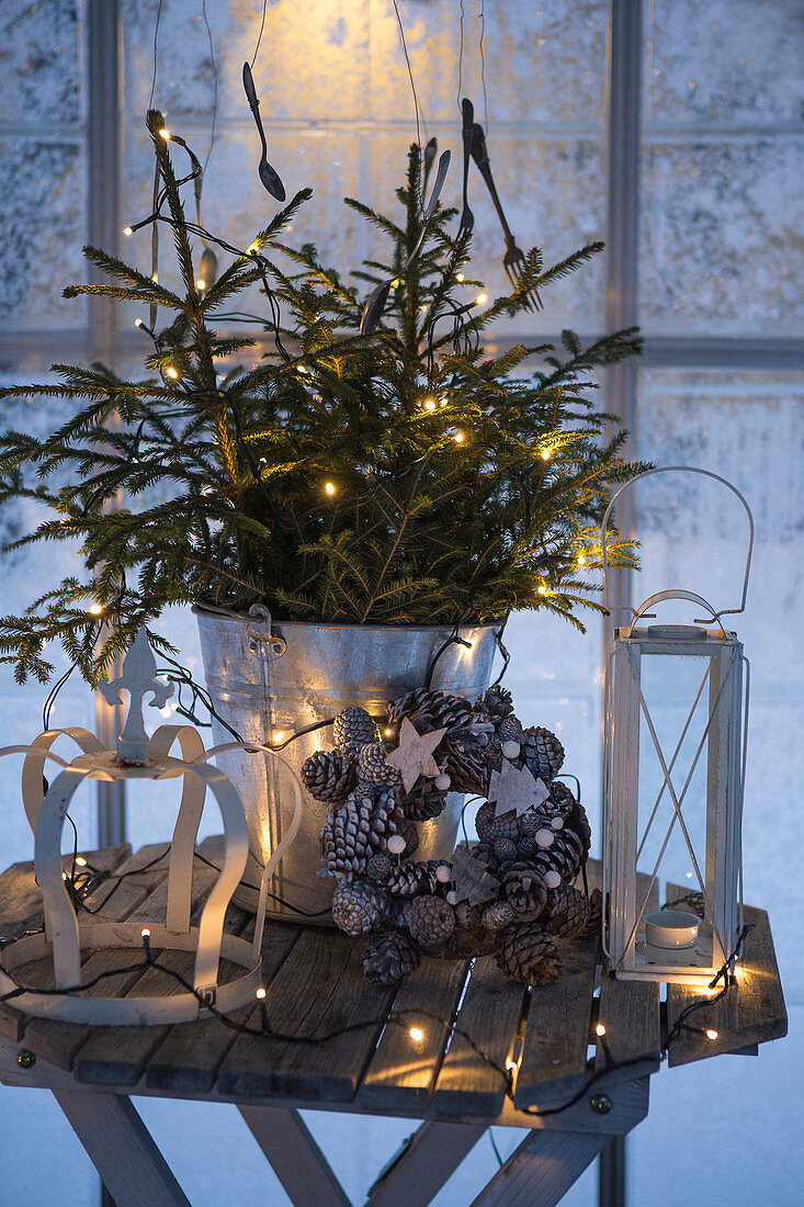 Weihnachtsdekoration mit Lichterkette auf Holztischchen vor Fenster