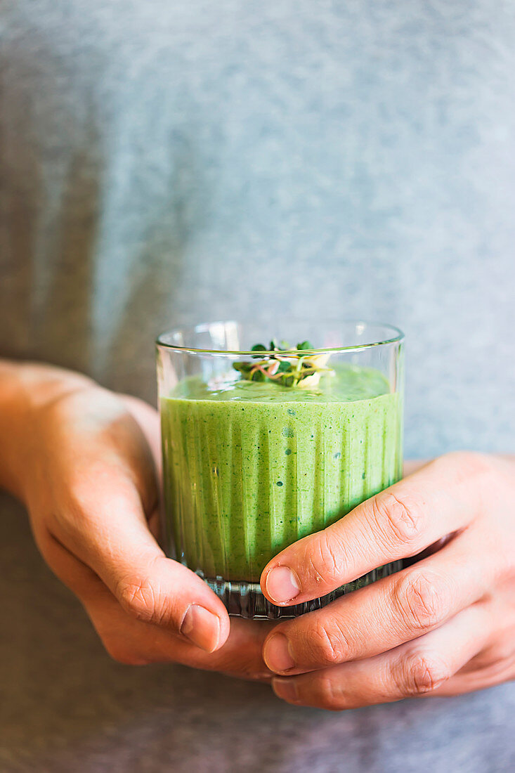 Green vegan smoothie with spinach, banana and sprouted seeds in glass in male hands