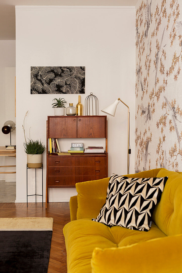Mustard-yellow sofa against patterned wallpaper and 50s cabinet in living room