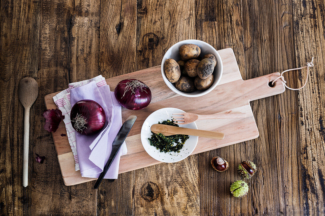 Kartoffeln, Kräuter und rote Zwiebeln auf Holzbrett