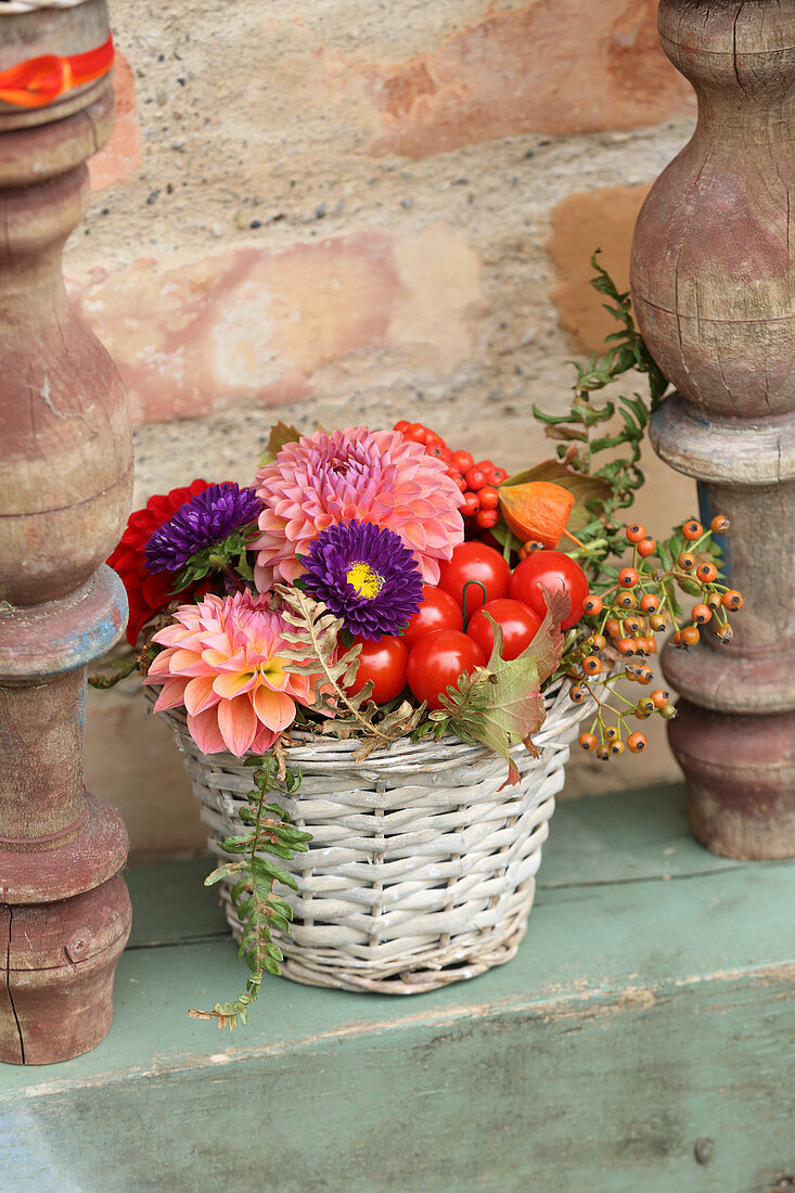 Buntes Gesteck mit Herbstblumen und Tomaten im Korb