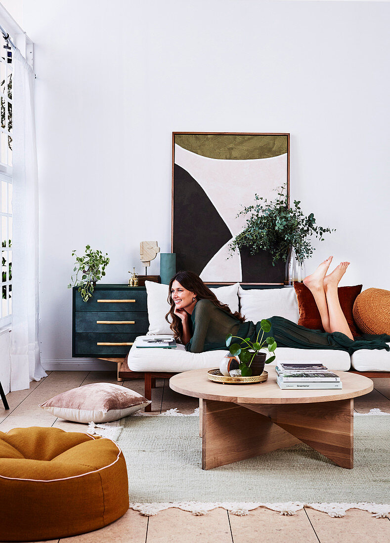 Couchtisch aus Holz, Sofa mit brünetter Frau, Zimmerpflanzen und Bild auf Sideboard im Wohnzimmer
