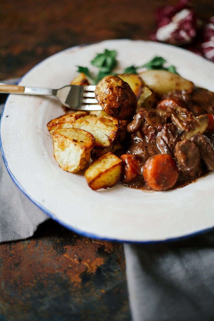 Beef bourguignon in ceramic plate with baked potatoes on metallic background