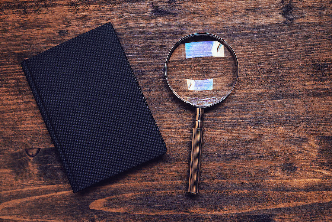 Magnifying glass and notebook on wooden desk