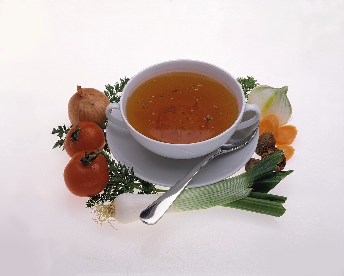 Vegetable broth in white soup cup, décor; fresh vegetables
