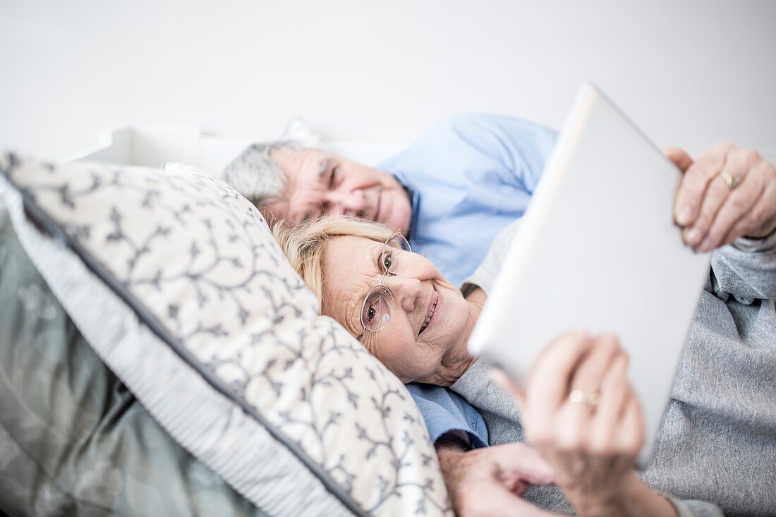 Senior couple lying down watching tablet
