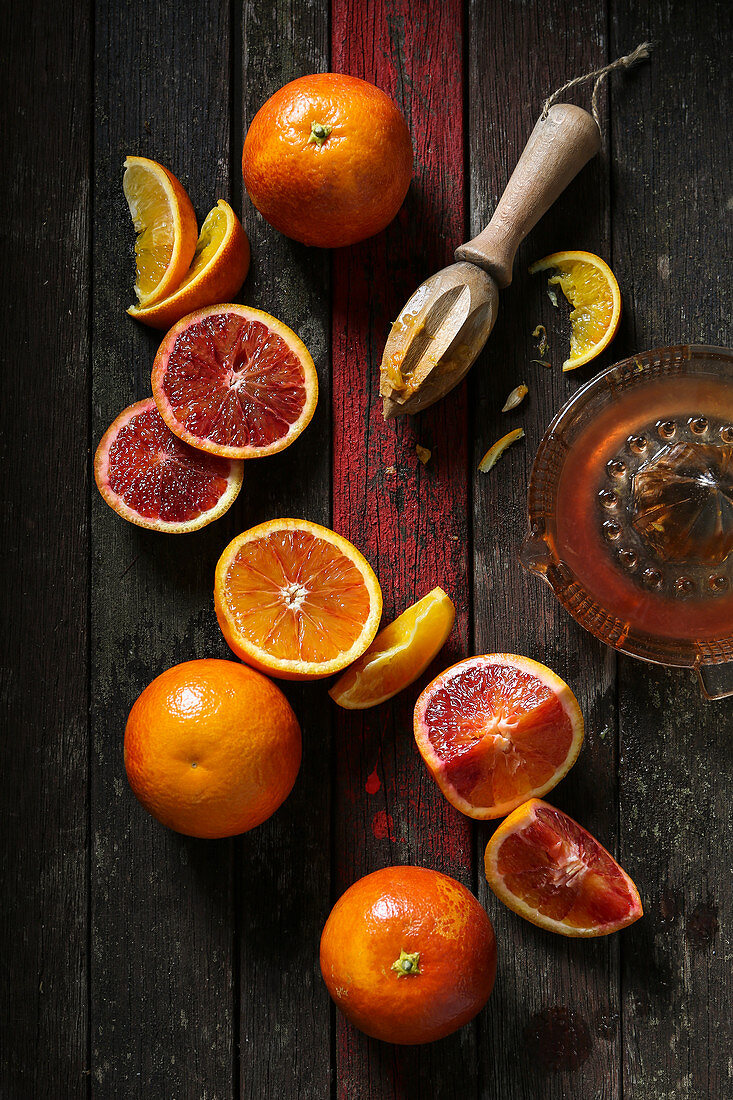 Blood oranges cut, halved, sliced and juiced with wooden juicing tool on rustic dark wooden background with red stripe