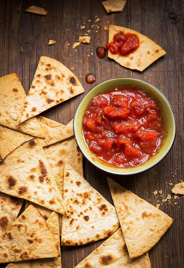 Small bowl and tomato salsa served with handmade tortilla chips on a rustic wooden board