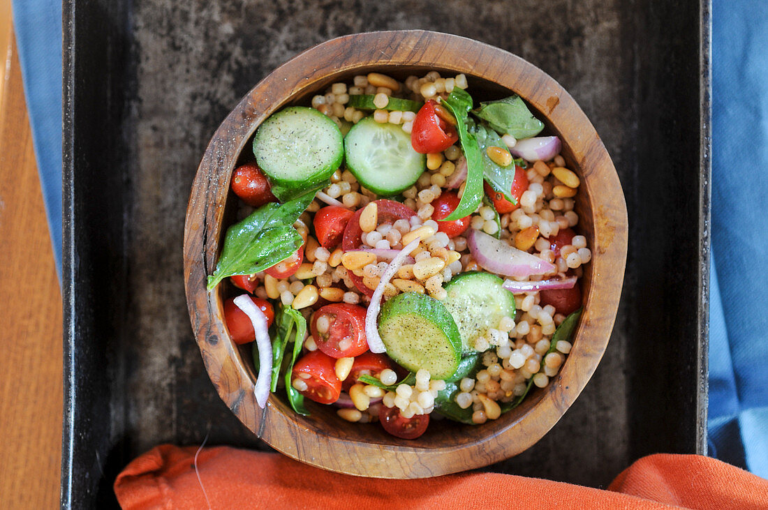 Israeli couscous salad with cucumbers, tomatoes and fresh basil in a wooden bowl