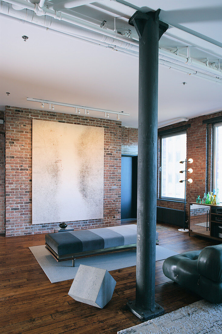 Lounger in different shades of grey in front of artwork in loft apartment with brick walls