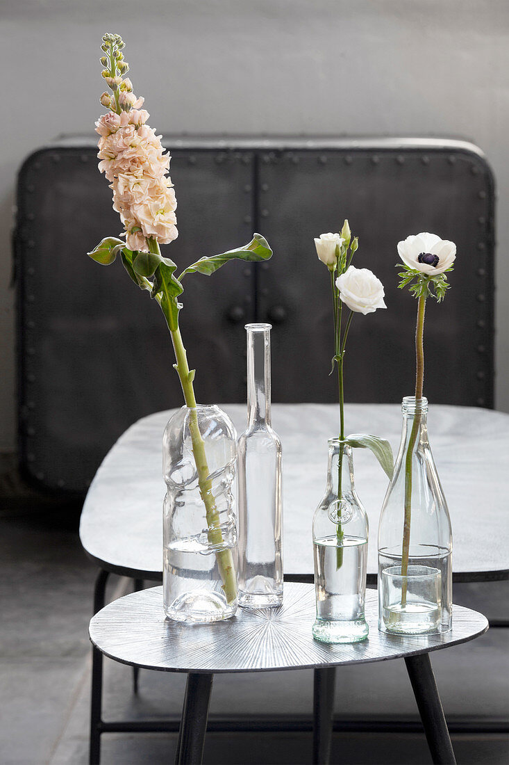 Verschiedene klare Glasflaschen als Blumenvasen auf einem Beistelltisch