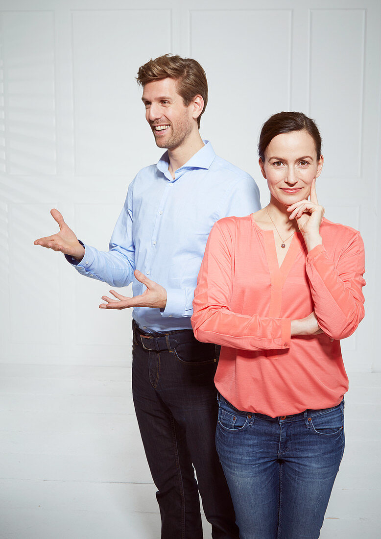 A smiling man standing behind a woman with her arms crossed