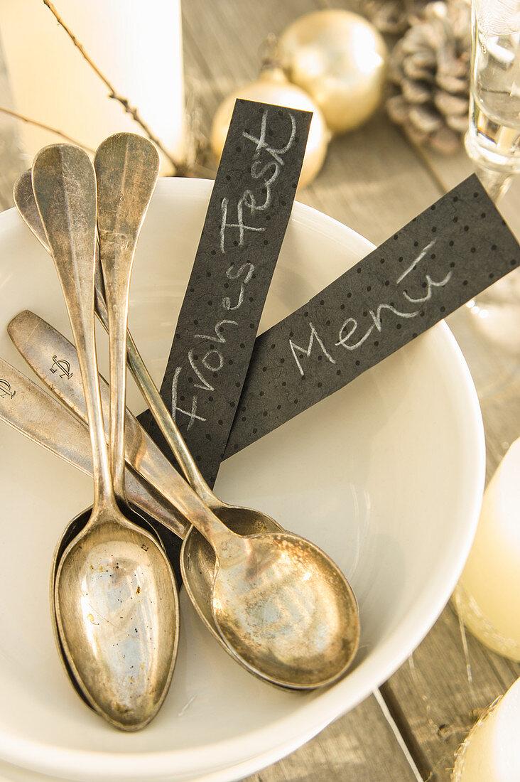 Old silver spoons and labels in a white bowl on a Christmas table