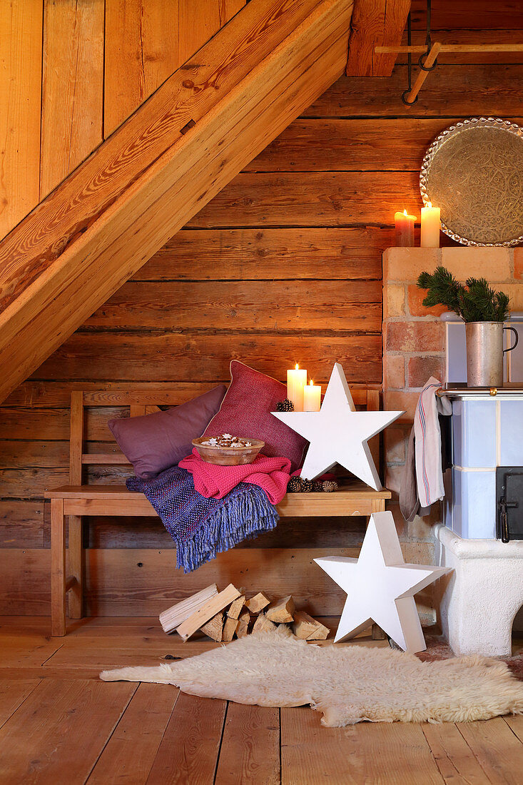 Kerzendekoration und Sterne in rustikaler Holzhütte mit Sitzbank neben Holzofen