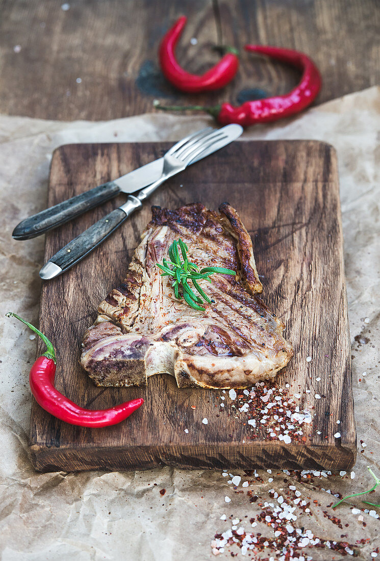 Cooked meat t-bone steak with red chili peppers, spices and fresh rosemary
