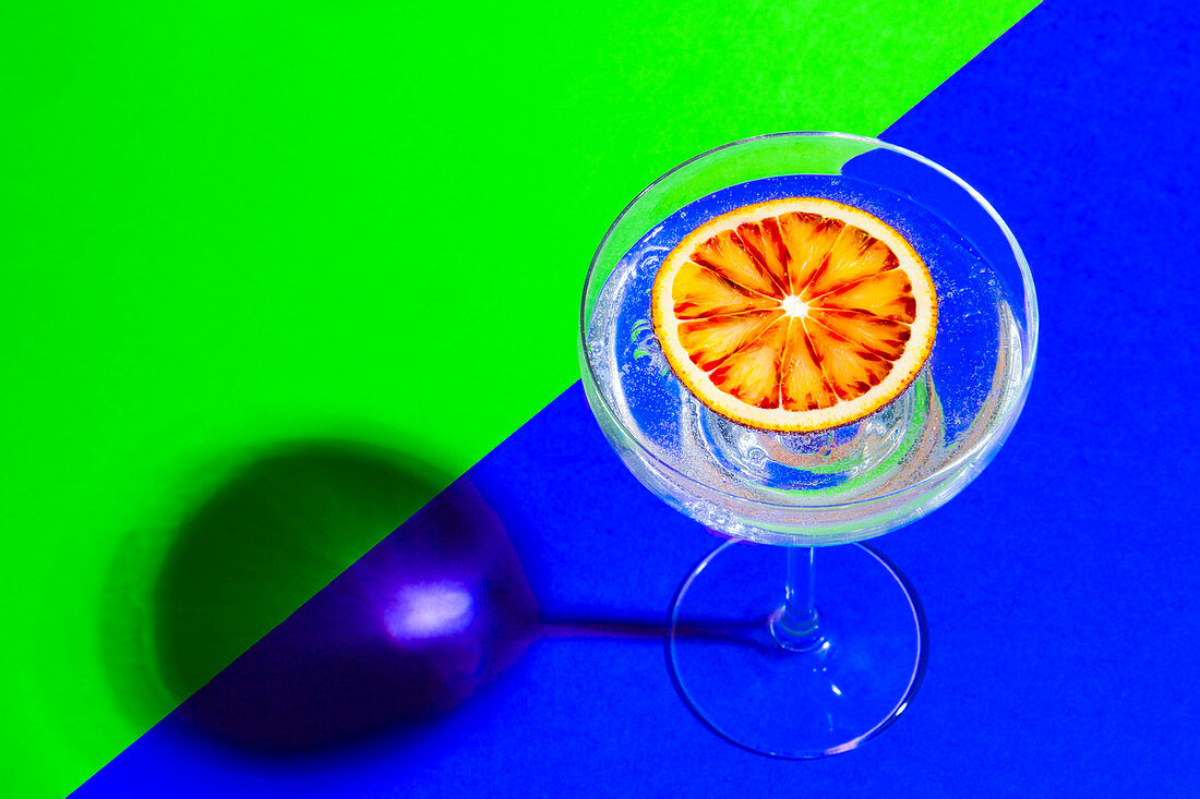 Blood orange slice in drink on green and blue backdrop