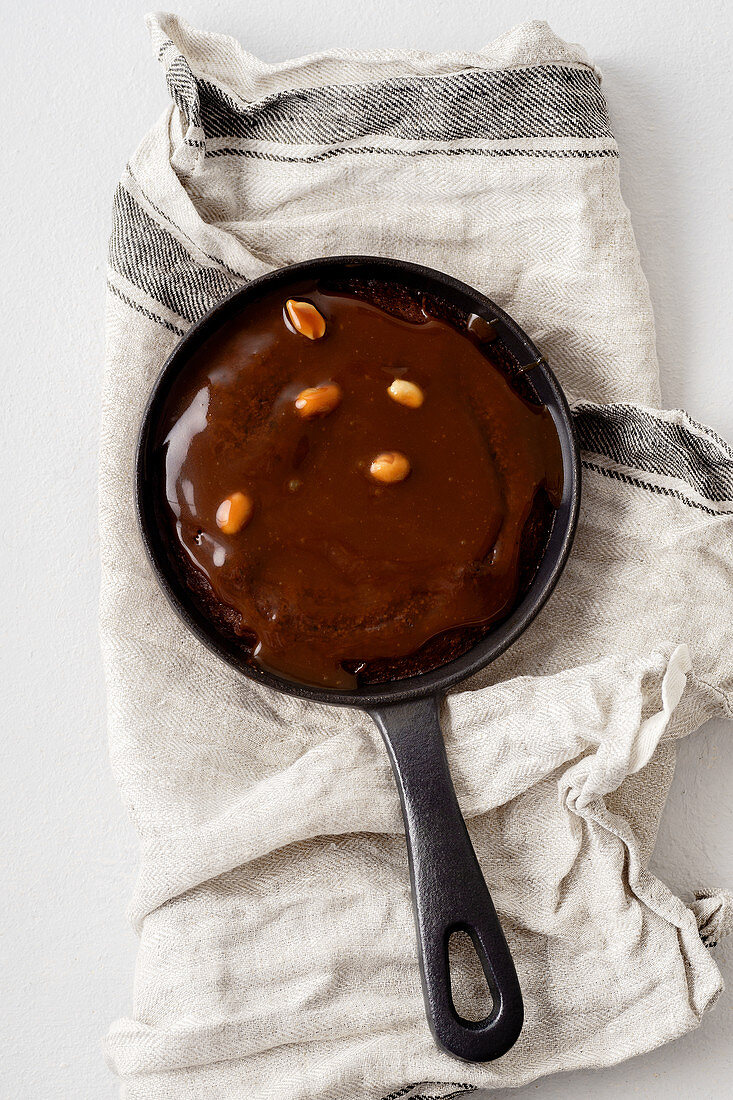 A brownie cake in a pan with salted caramel and roasted peanuts