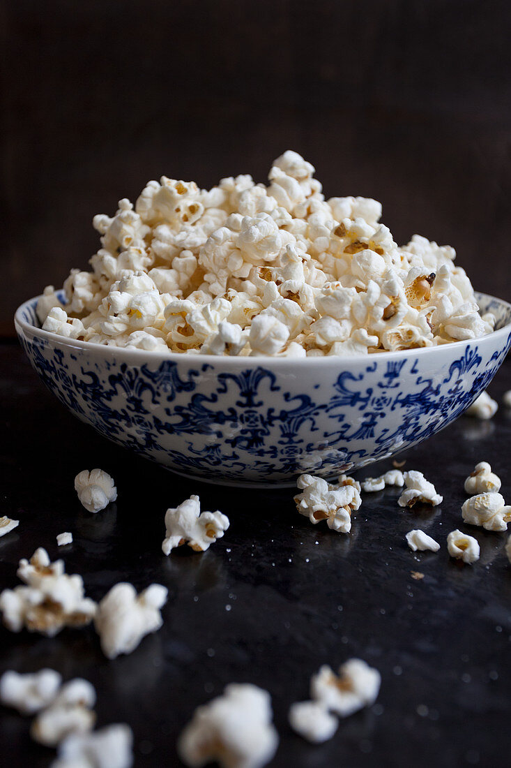 Popcorn in a blue and white bowl, spilling onto a black countertop