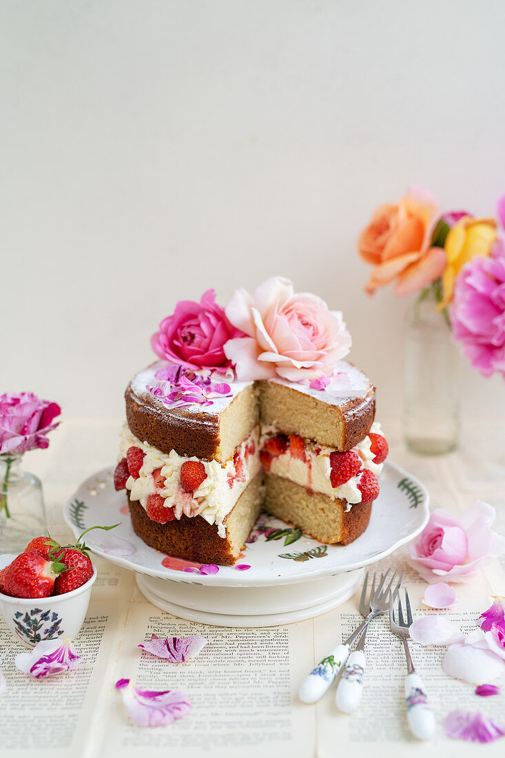 Strawberry rose layer cake topped with roses on a cake stand, slice taken out