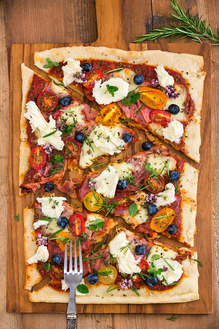 Pizza with mozzarella, tomatoes, ham, blueberries, rosemary, oregano and thyme