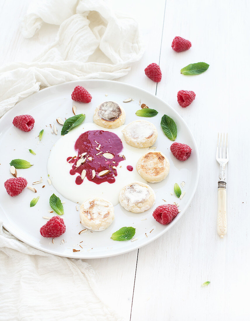 Russian cottage cheese cakes with berry jam, almonds, fresh raspberries and mint over