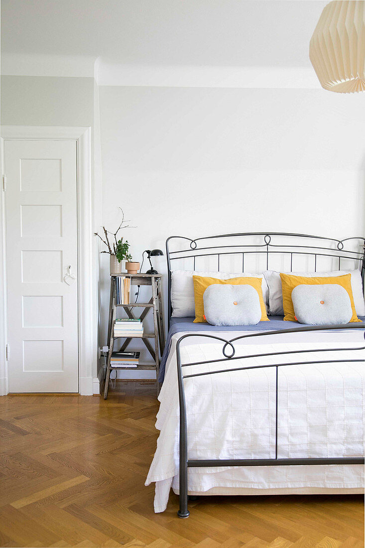 Step ladders used as bedside table next to metal bed in bedroom