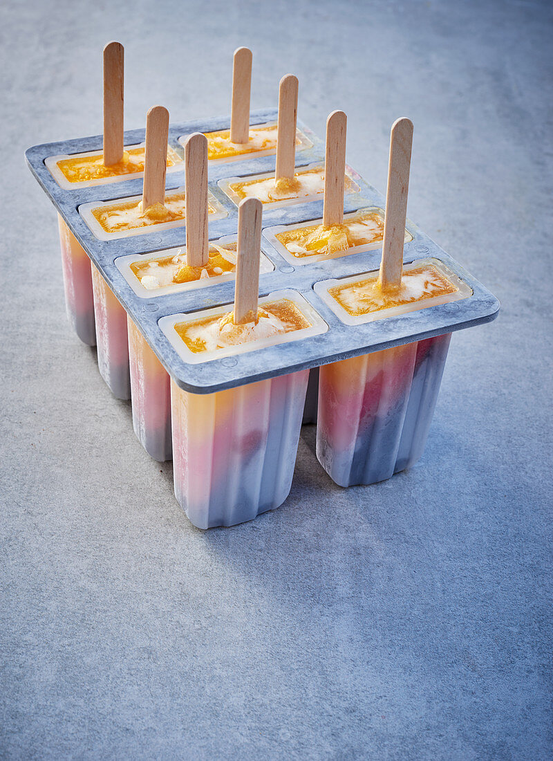 Tri-coloured ice cream sticks in lolly moulds on a grey surface