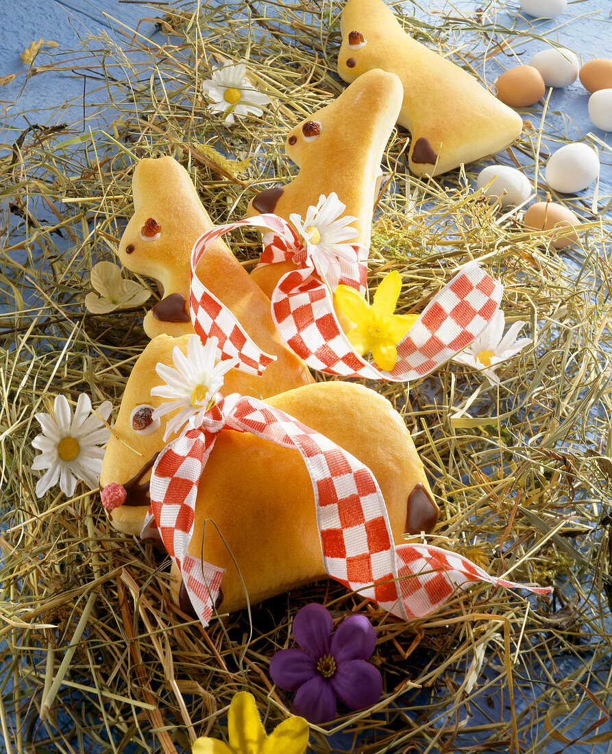 Sweet yeast dough Easter bunnies on hay with spring flowers
