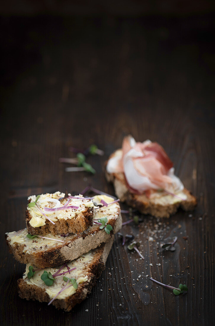 Buttered bread topped with herbs and shallots, and one topped with cured ham
