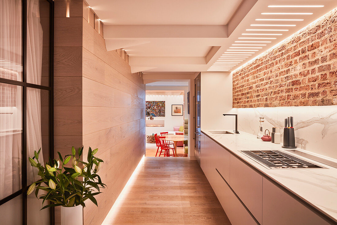 Long, narrow kitchen with brick wall leading into dining room