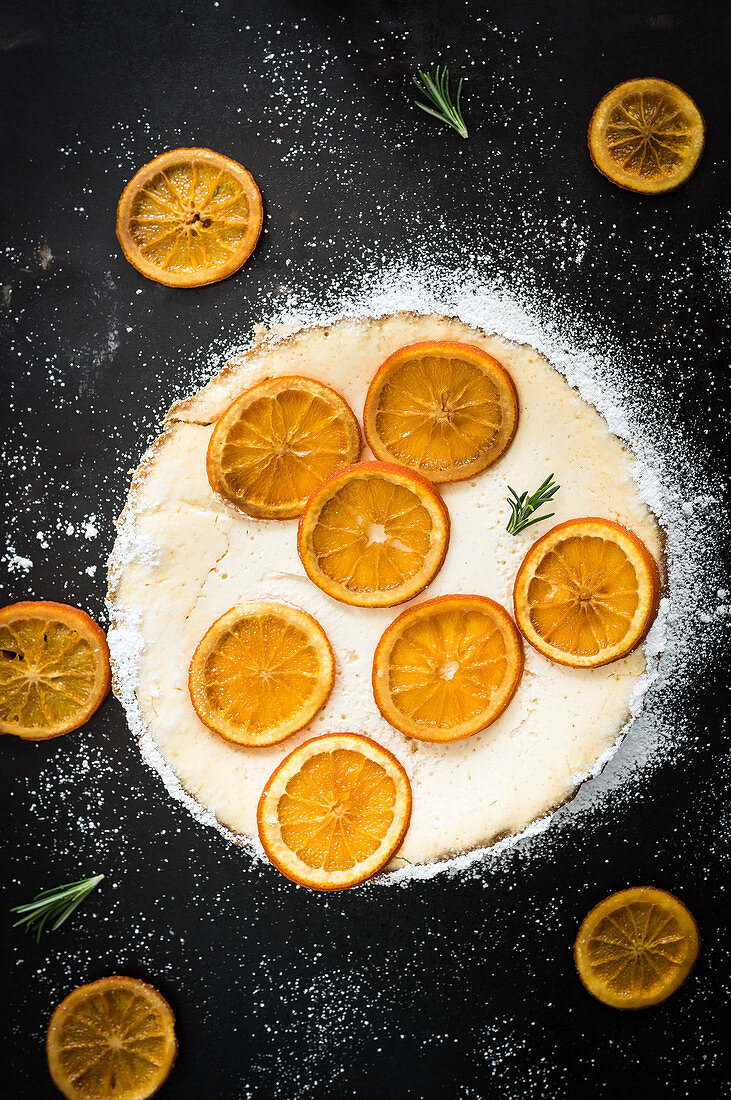 Orange tart with orange slices, yoghurt cream, rosemary and icing sugar