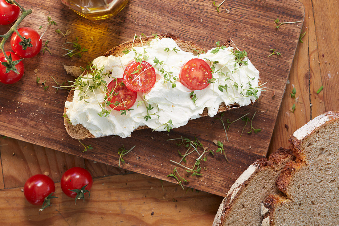 A slice of bread topped with cream cheese, tomatoes and cress