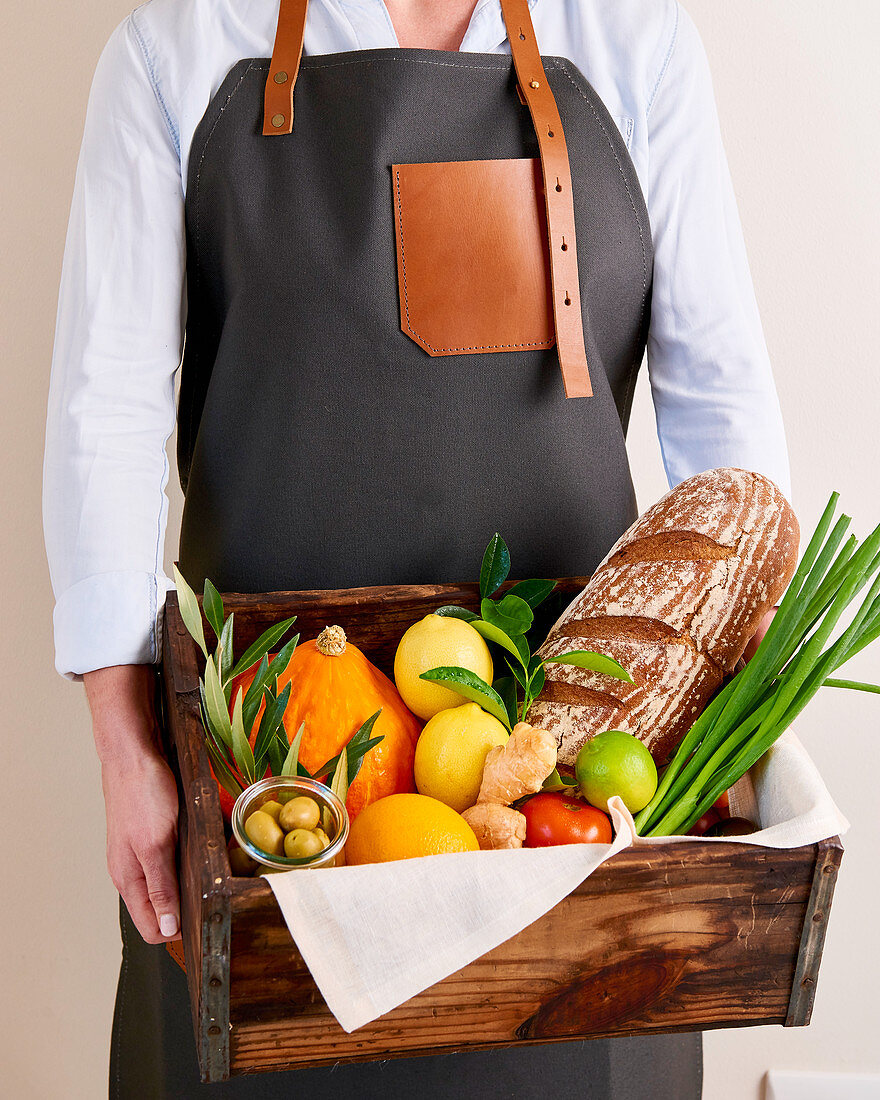 Mann hält eine Holzkiste mit frischem Obst, Gemüse und Brot