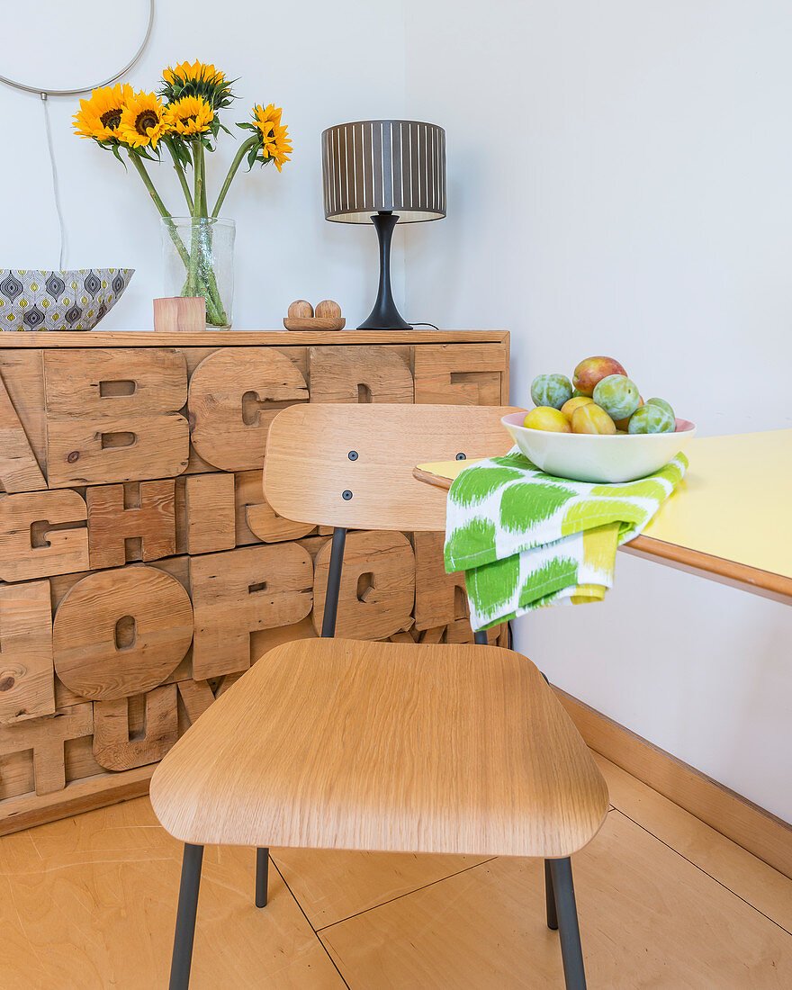 Chair at dining table in front of chest of drawers with carved letters on front