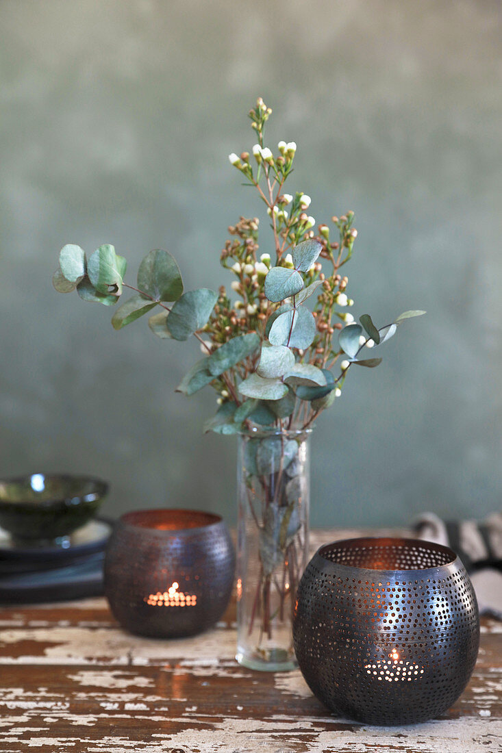 Windlichter neben einer Vase mit Eukalyptus und Wachsblumen