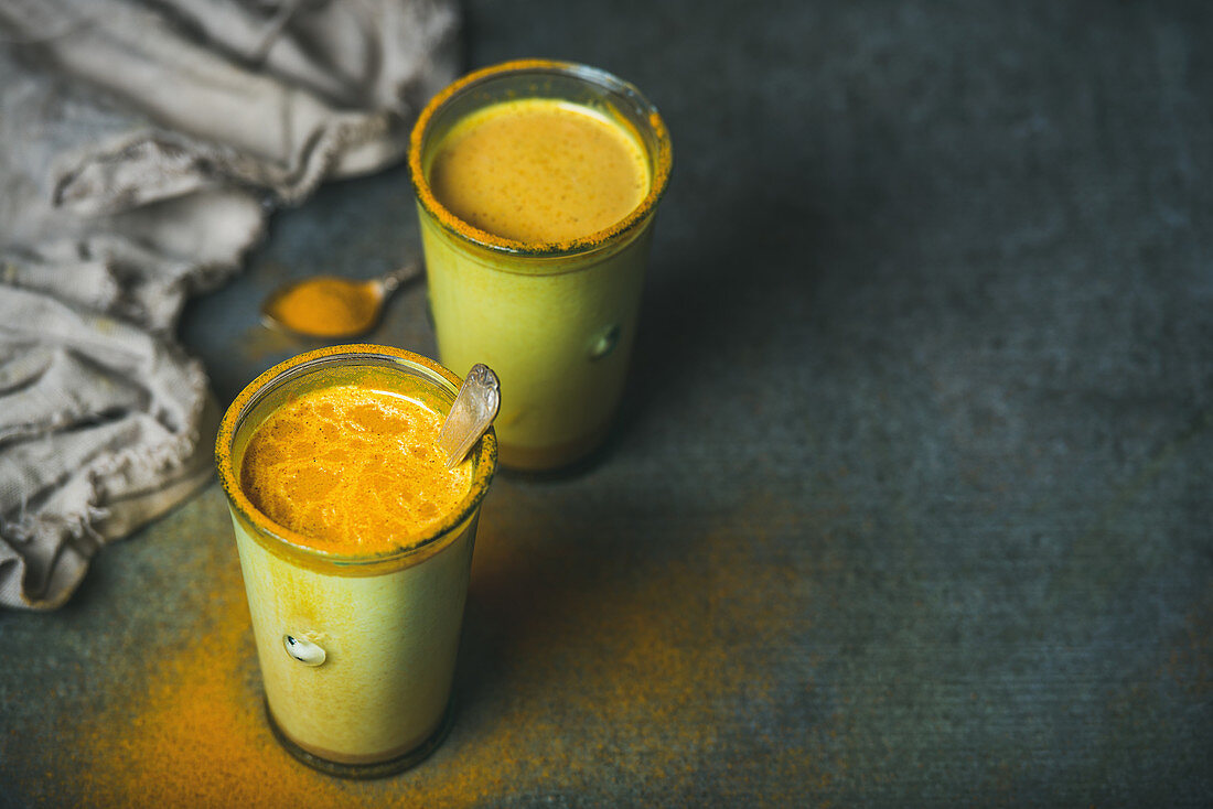 Golden milk with turmeric powder in glasses over dark grunge background