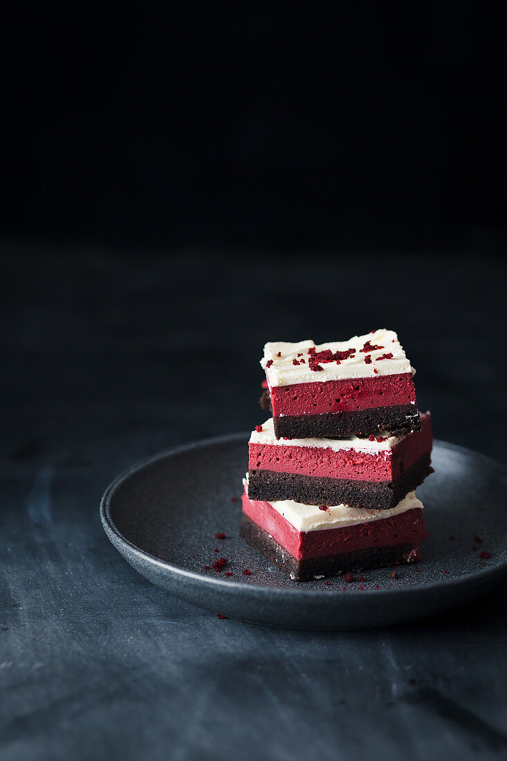 Red Velvet Cheesecake-Brownies auf Teller vor schwarzem Hintergrund