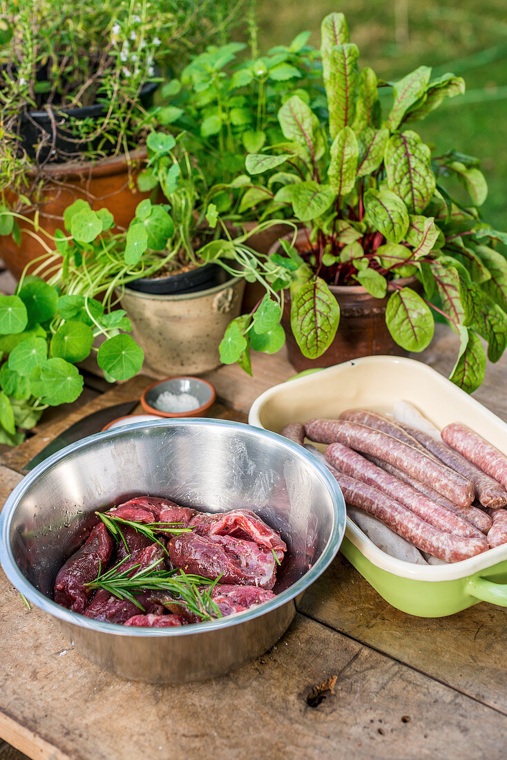 Sausages and marinated meat for grilling on a wooden board in a garden kitchen
