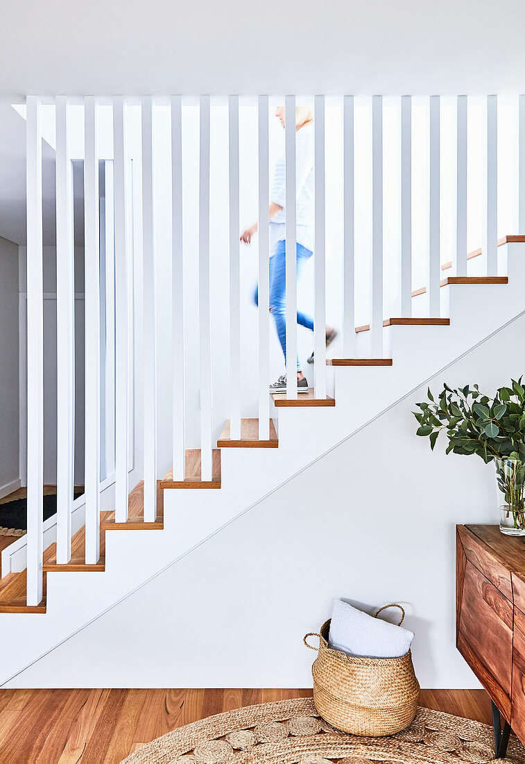 Staircase with straight white balusters, vase of leaves on sideboard and basket on floor