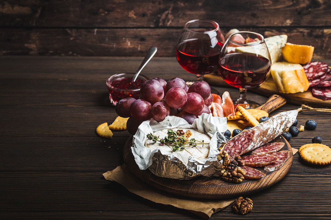 A platter of cheese, meat, crackers, bread, grapes and nuts with red wine