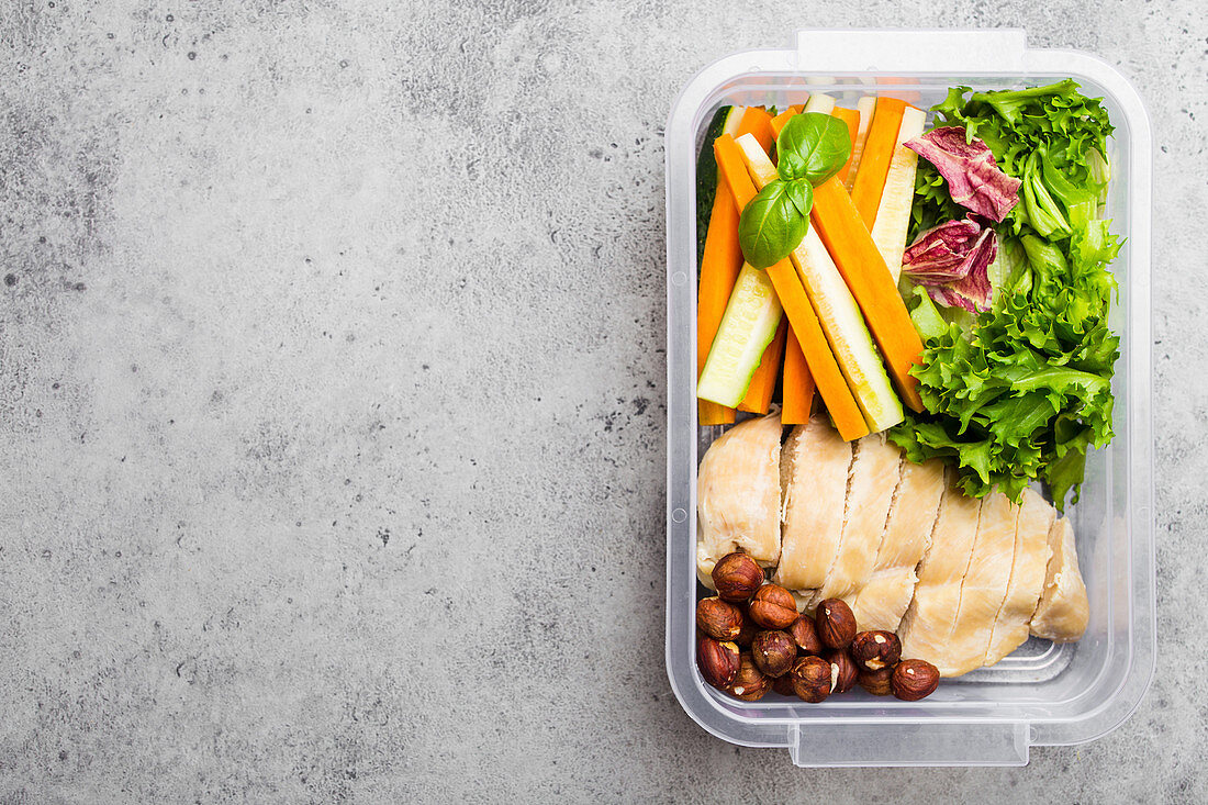 A healthy lunchbox with chicken breast, nuts, salad and vegetables sticks