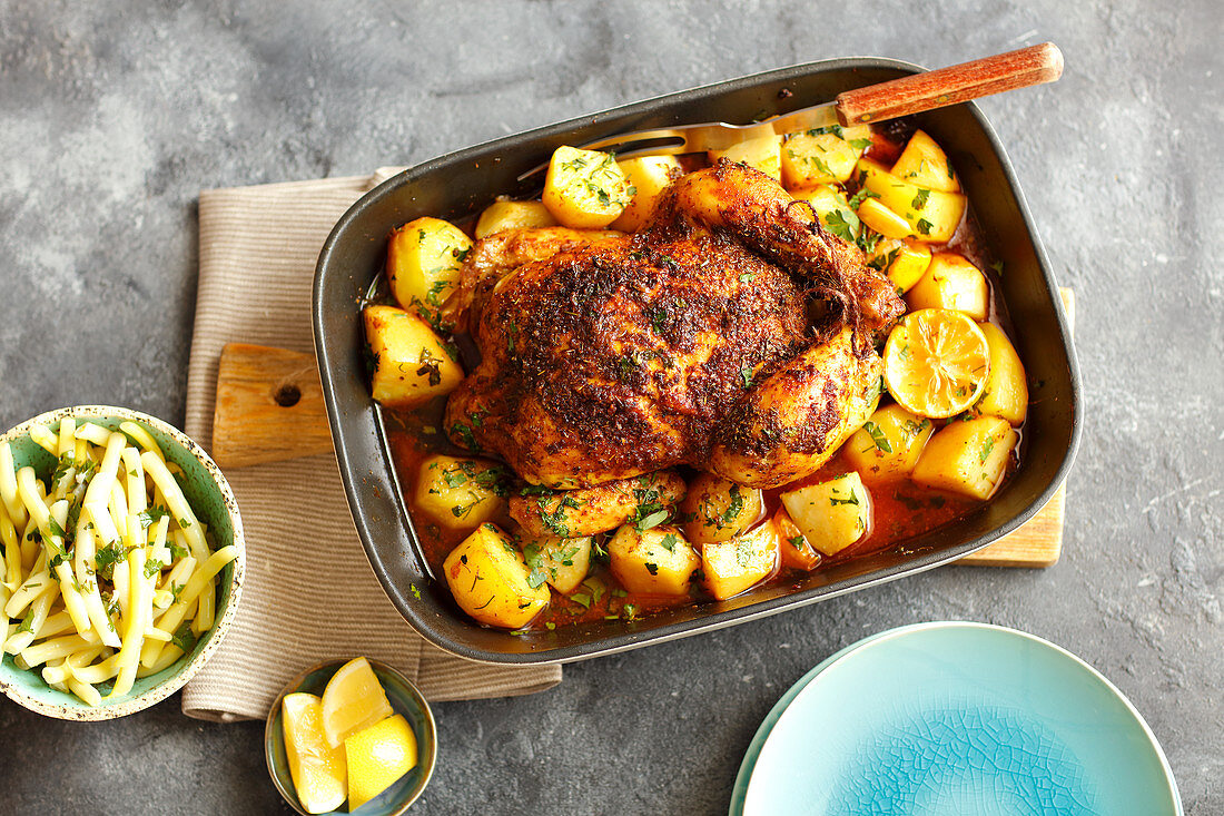 Roast chicken with potatoes and lemons in a baking tin (seen from above)