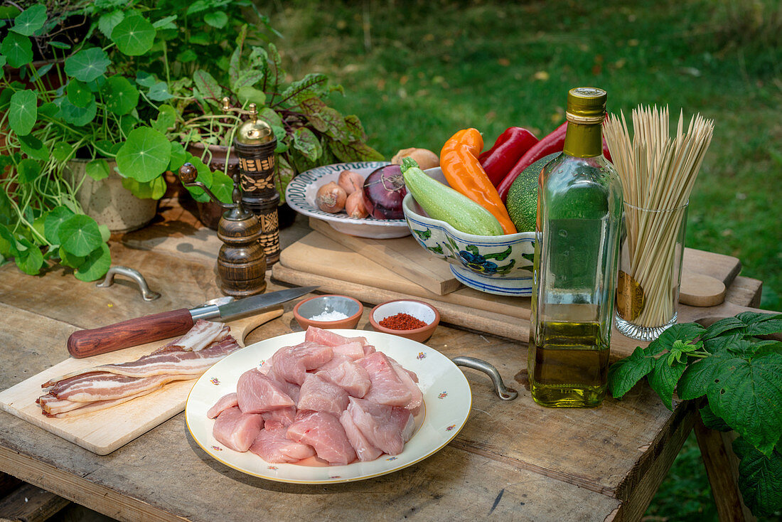 Ingredients for barbecue skewers with pork, bacon and vegetables on a wooden table in a garden
