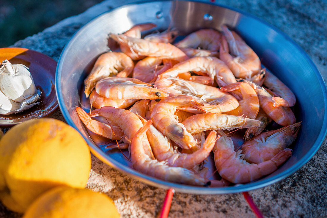 Fresh prawns in a pan with lemon and garlic on a stone surface