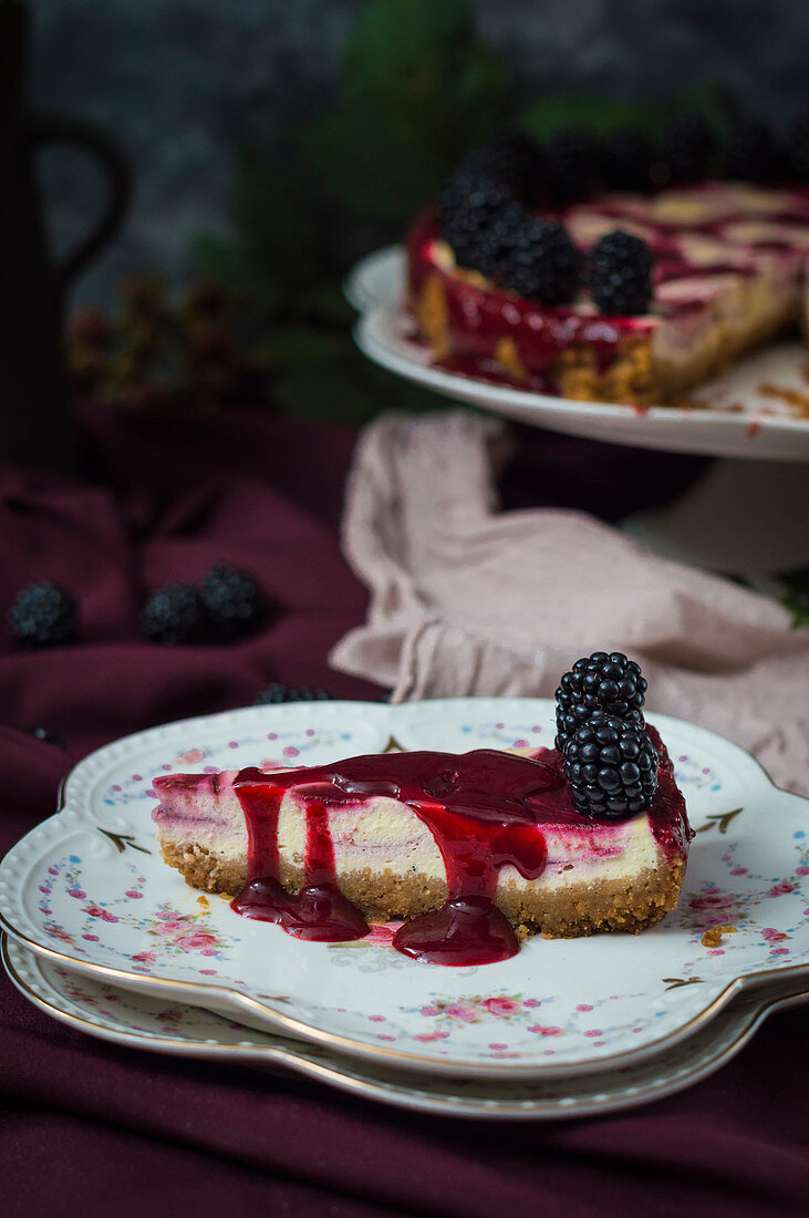 Slice of blackberry cheesecake on floral plate drizzled with blackberry sauce