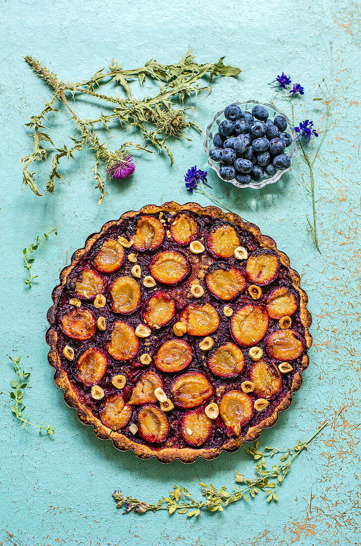 Pie with plums and hazelnuts on a blue background with herbarium and fresh blueberries