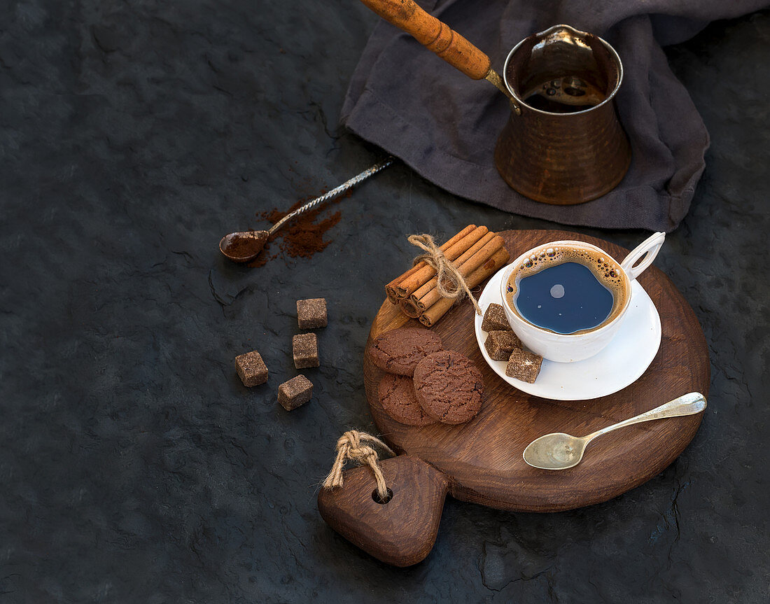 Cup of black coffee with chocolate biscuits, cinnamon sticks and cane sugar cubes